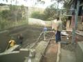 Pool being sprayed with concrete. A concrete pump was used to bring in the mix. Note the drop-sheets to stop overspray. The foreground shows the freshly sprayed concrete retaining wall between the pool area and patio above.
